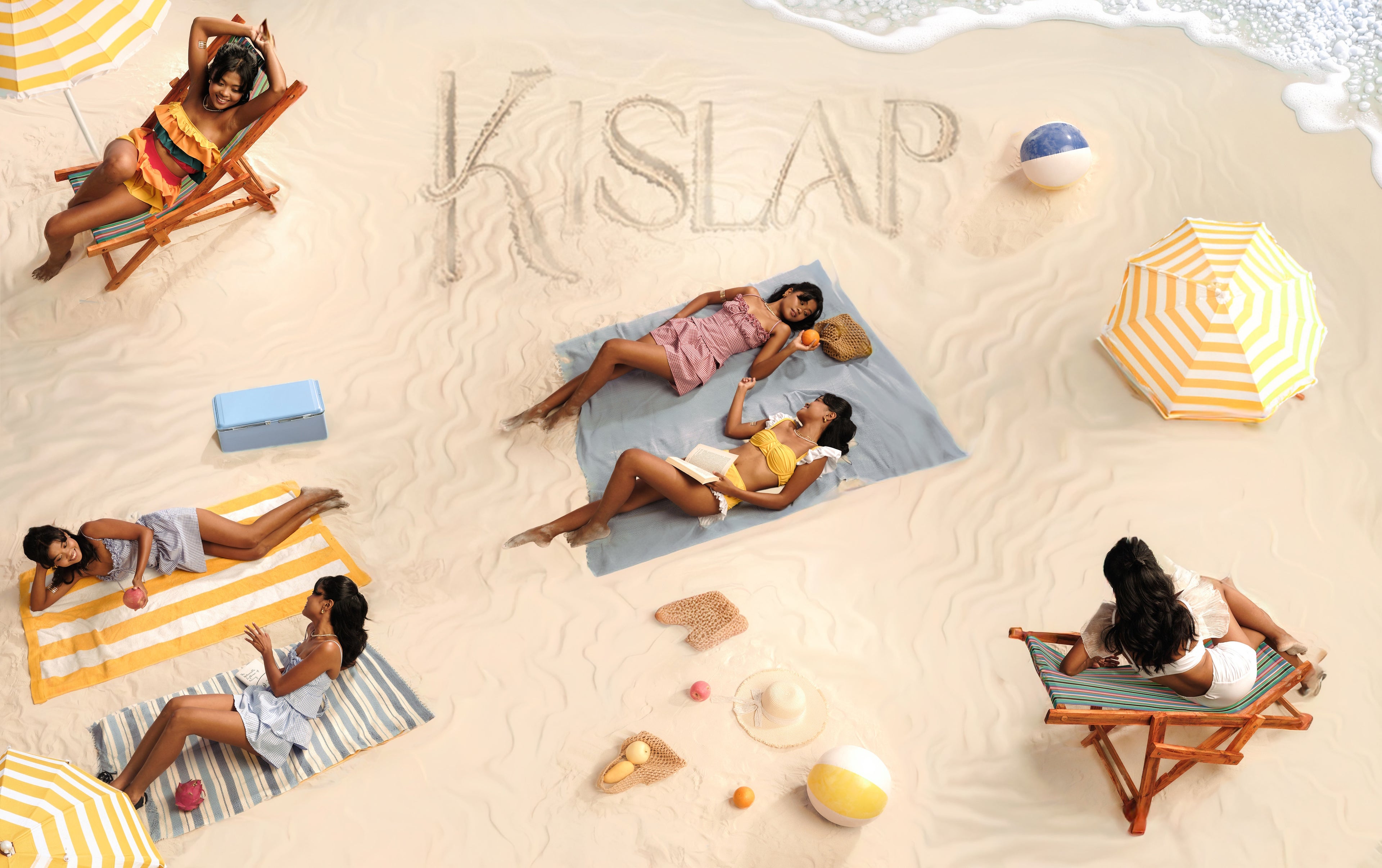 An overhead beach scene with several women relaxing on towels and deck chairs on sand, with yellow-and-white umbrellas and the word 'KISLAP' written in the sand.